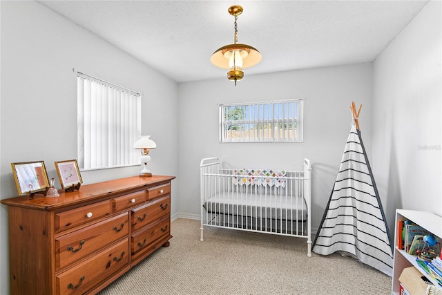 bedroom featuring light carpet, a nursery area, and a textured ceiling