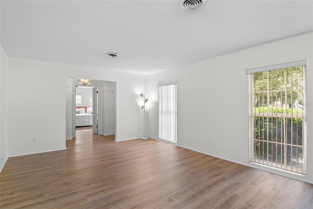 spare room featuring baseboards, a notable chandelier, light wood finished floors, and visible vents