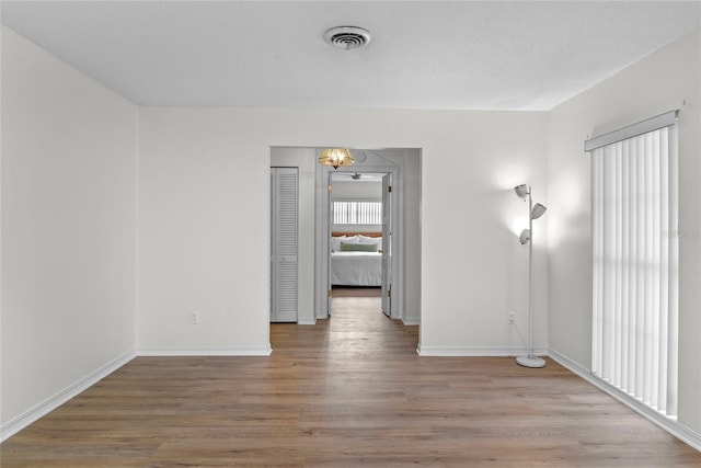 empty room with visible vents, light wood-style flooring, baseboards, and a chandelier