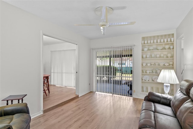 living area featuring a ceiling fan, baseboards, built in features, and wood finished floors