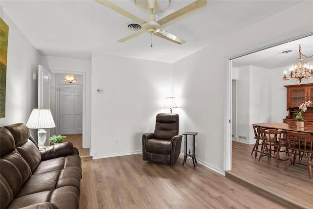living area with light wood-style floors, baseboards, and ceiling fan with notable chandelier