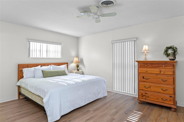 bedroom featuring baseboards, ceiling fan, wood finished floors, and visible vents