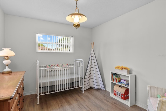 bedroom featuring baseboards, a crib, and wood finished floors