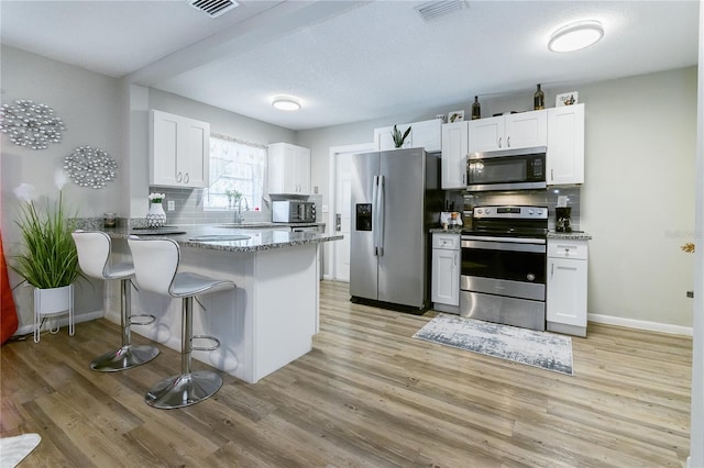 kitchen featuring appliances with stainless steel finishes, kitchen peninsula, light stone countertops, decorative backsplash, and white cabinets