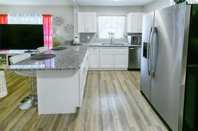 kitchen featuring sink, a breakfast bar area, white cabinetry, stainless steel appliances, and decorative backsplash