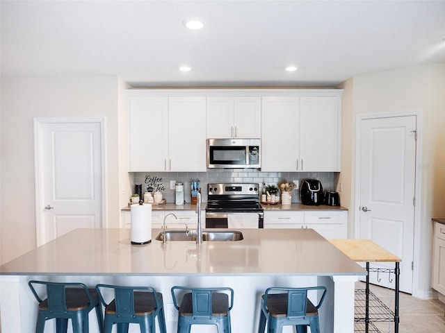 kitchen with a breakfast bar, sink, stainless steel appliances, a kitchen island with sink, and white cabinets