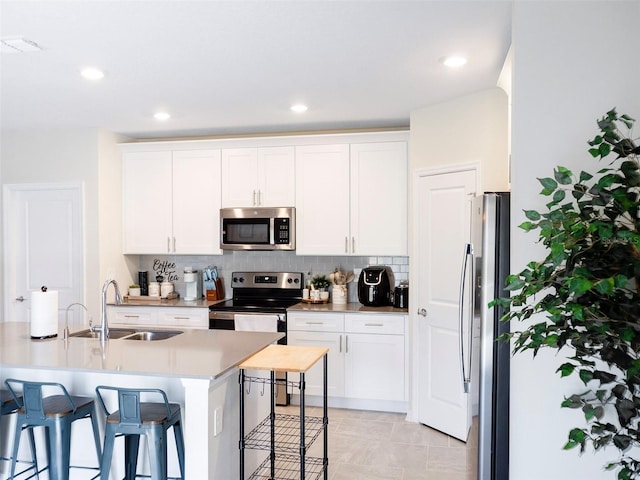 kitchen with white cabinetry, stainless steel appliances, a kitchen bar, and sink