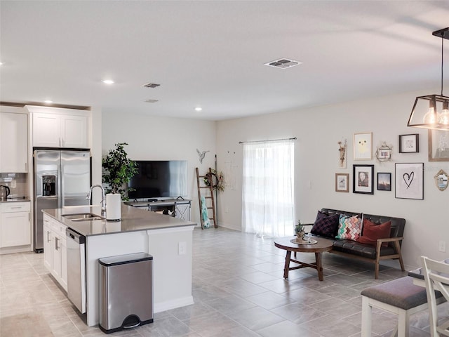 kitchen featuring pendant lighting, sink, white cabinetry, stainless steel appliances, and a center island with sink