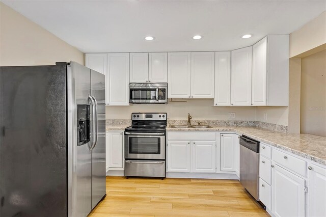 kitchen with sink, light hardwood / wood-style flooring, appliances with stainless steel finishes, light stone countertops, and white cabinets