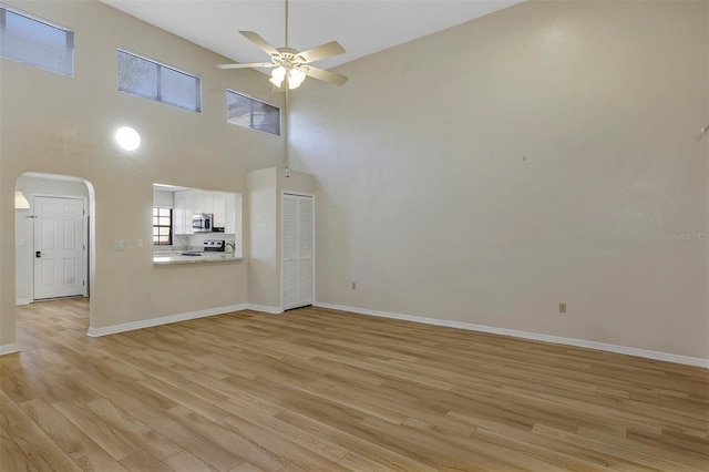 unfurnished living room with a high ceiling, ceiling fan, and light hardwood / wood-style flooring