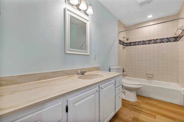 full bathroom with vanity, tiled shower / bath, hardwood / wood-style floors, and toilet