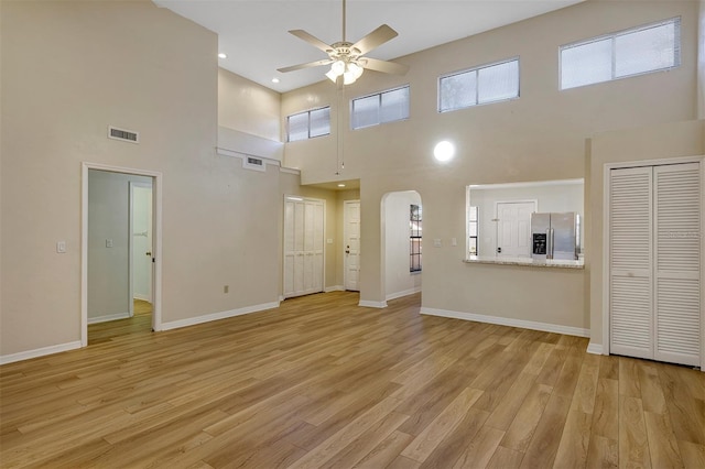 unfurnished living room with light hardwood / wood-style floors, ceiling fan, and a high ceiling