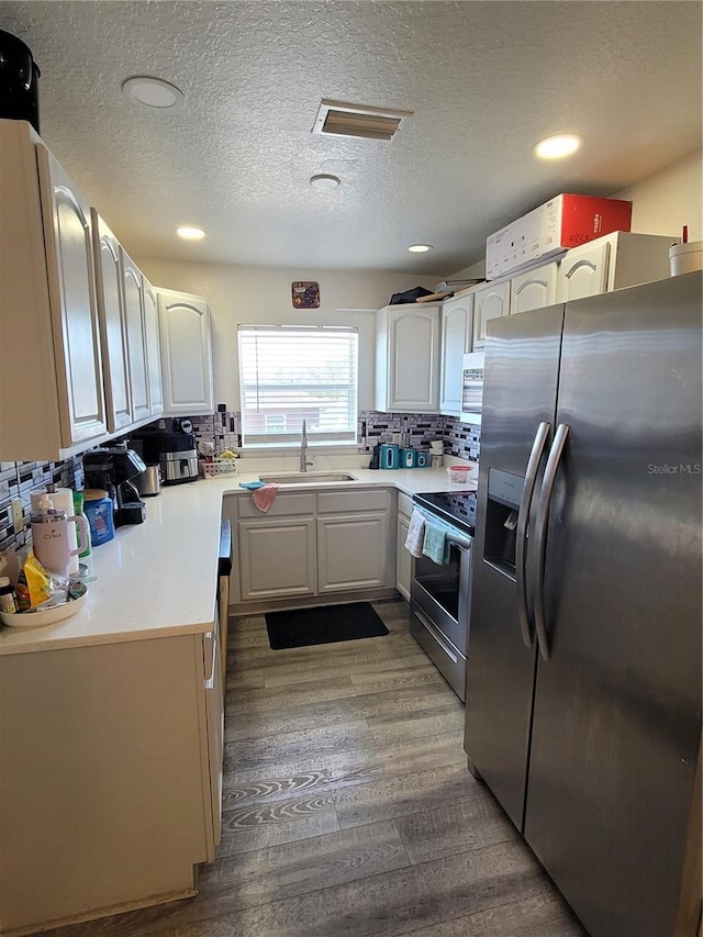 kitchen featuring sink, tasteful backsplash, white cabinetry, wood-type flooring, and stainless steel appliances