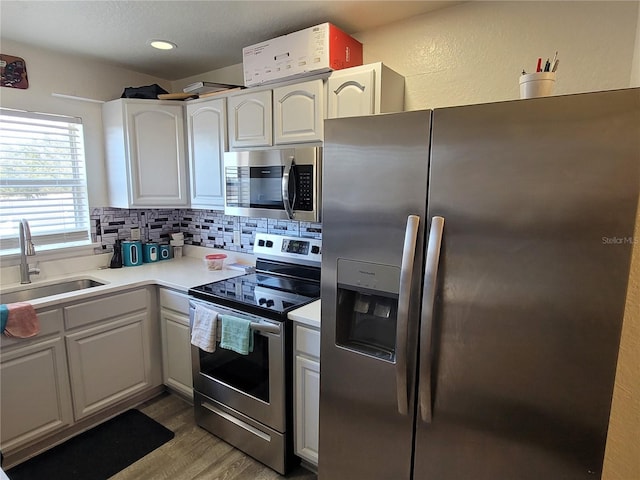 kitchen with wood-type flooring, sink, white cabinets, decorative backsplash, and stainless steel appliances