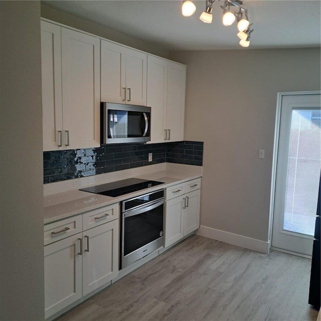 kitchen with backsplash, stainless steel appliances, white cabinets, and light wood-type flooring