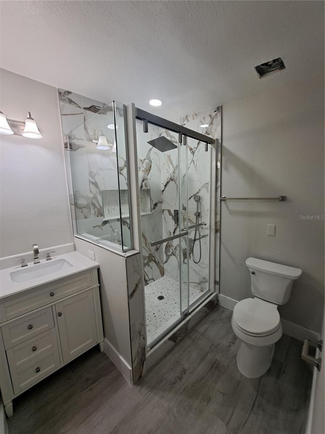 bathroom with wood-type flooring, vanity, walk in shower, toilet, and a textured ceiling