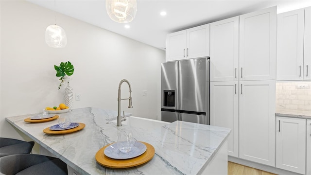 kitchen with white cabinetry, stainless steel refrigerator with ice dispenser, backsplash, and decorative light fixtures