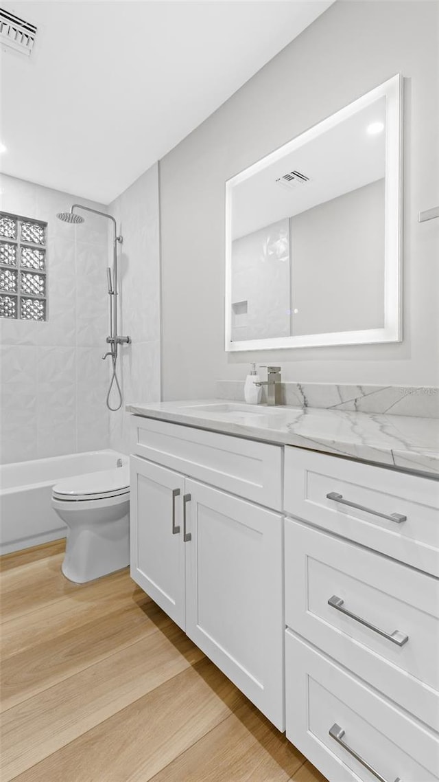 full bathroom featuring vanity, tiled shower / bath, wood-type flooring, and toilet