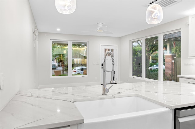 kitchen featuring pendant lighting, white cabinetry, sink, ceiling fan, and light stone counters