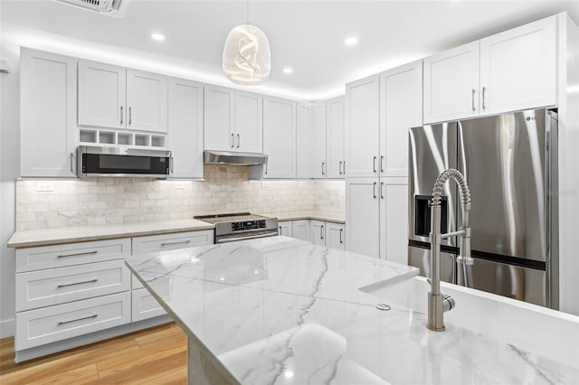 kitchen featuring backsplash, hanging light fixtures, stainless steel appliances, light stone countertops, and light wood-type flooring