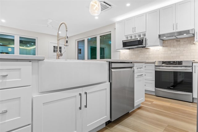 kitchen with white cabinetry, backsplash, light hardwood / wood-style flooring, and appliances with stainless steel finishes