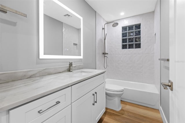 full bathroom with vanity, tiled shower / bath, hardwood / wood-style floors, and toilet