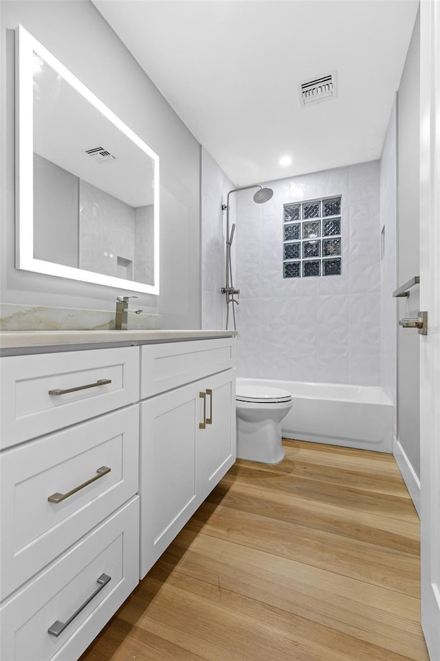 full bathroom with vanity, tiled shower / bath, hardwood / wood-style flooring, and toilet