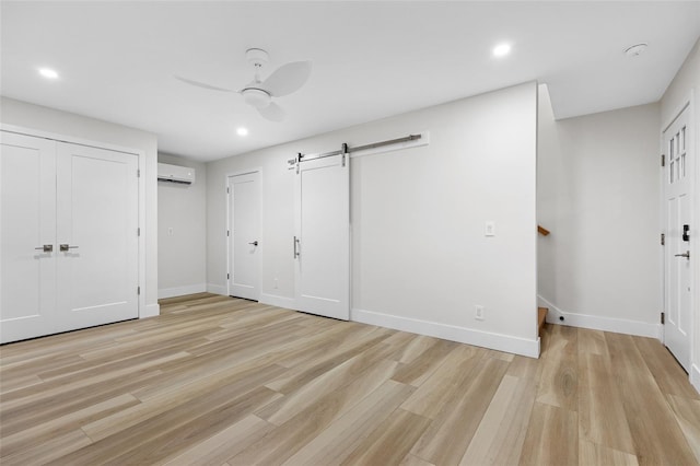 unfurnished bedroom with a barn door, a wall mounted AC, ceiling fan, and light hardwood / wood-style flooring