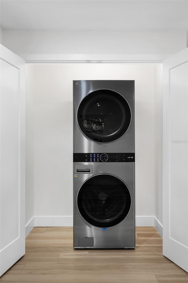 clothes washing area featuring stacked washing maching and dryer and light wood-type flooring