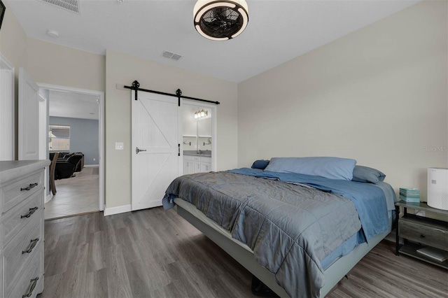 bedroom with a barn door, hardwood / wood-style floors, and ensuite bath