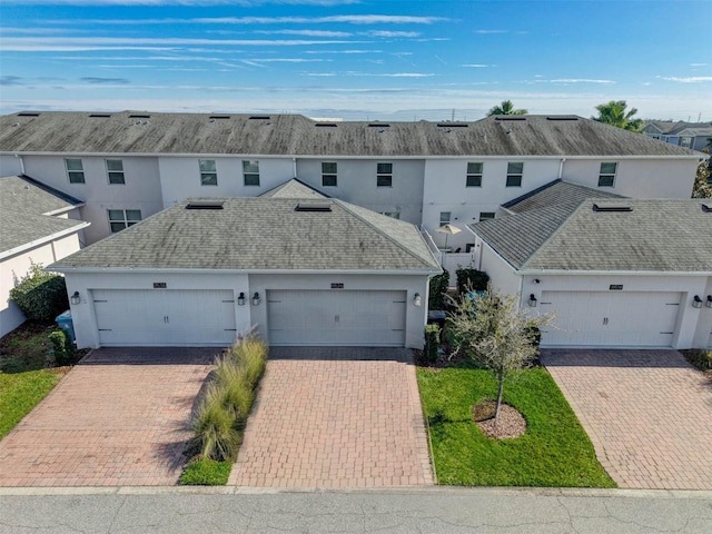 view of front of property with stucco siding, a shingled roof, and decorative driveway
