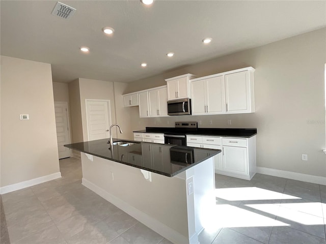 kitchen with sink, a breakfast bar area, stainless steel appliances, white cabinets, and a center island with sink