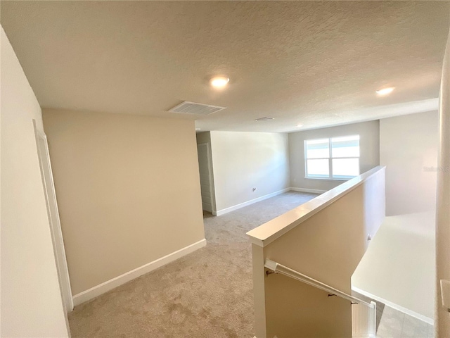 hallway featuring light carpet and a textured ceiling