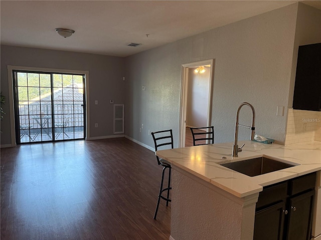 kitchen with sink, light stone counters, a kitchen bar, dark hardwood / wood-style flooring, and kitchen peninsula