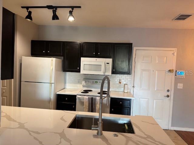 kitchen featuring light stone countertops, sink, backsplash, and white appliances