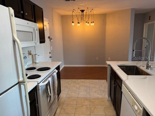 kitchen featuring light tile patterned flooring, pendant lighting, sink, a notable chandelier, and white appliances