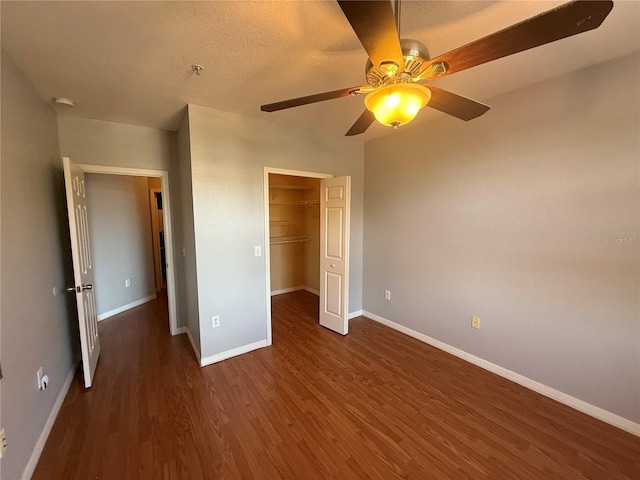 unfurnished bedroom featuring a spacious closet, a textured ceiling, dark hardwood / wood-style flooring, a closet, and ceiling fan