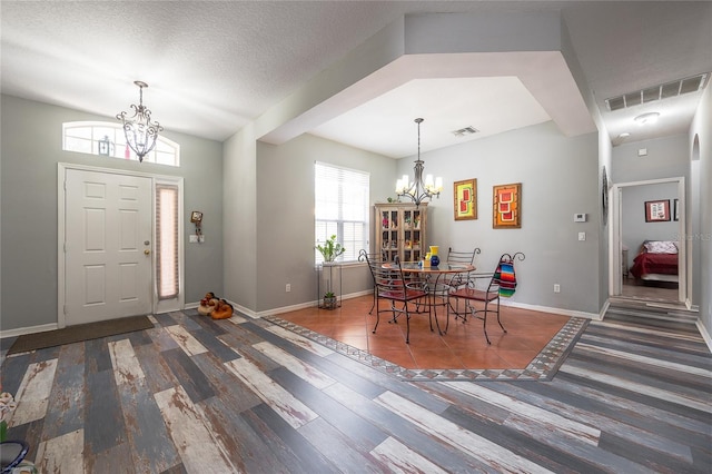 entrance foyer with a textured ceiling, visible vents, and an inviting chandelier