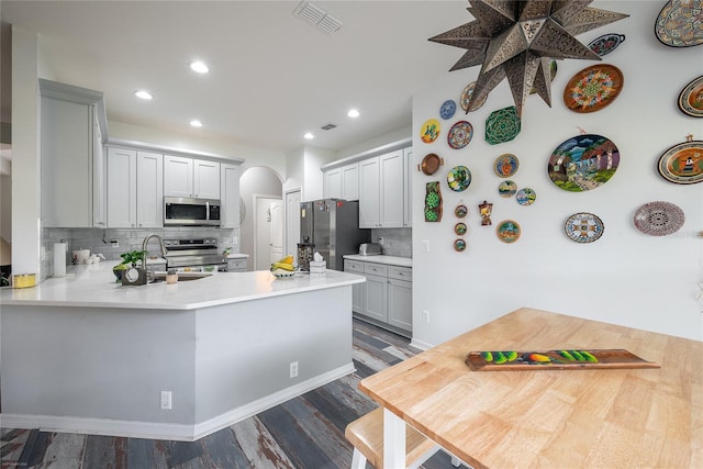 kitchen featuring dark wood-type flooring, sink, tasteful backsplash, appliances with stainless steel finishes, and kitchen peninsula