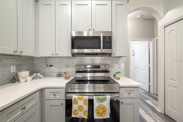 kitchen with tasteful backsplash, appliances with stainless steel finishes, gray cabinetry, and light hardwood / wood-style flooring