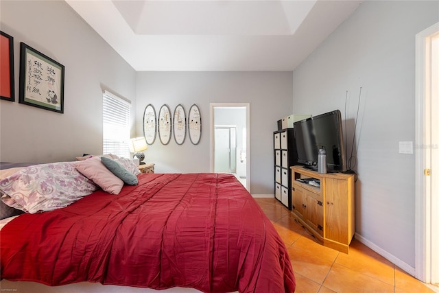 bedroom featuring a tray ceiling, connected bathroom, baseboards, and light tile patterned floors