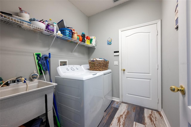 clothes washing area featuring a sink, separate washer and dryer, wood finished floors, laundry area, and baseboards