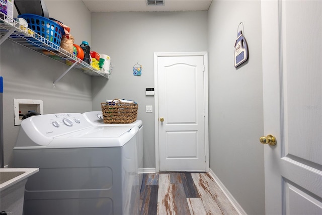 laundry room featuring laundry area, separate washer and dryer, a sink, wood finished floors, and visible vents