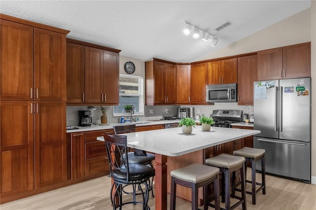 kitchen with appliances with stainless steel finishes, a kitchen island, light hardwood / wood-style floors, a kitchen bar, and vaulted ceiling