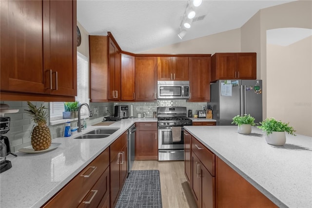 kitchen with vaulted ceiling, appliances with stainless steel finishes, tasteful backsplash, sink, and light stone countertops