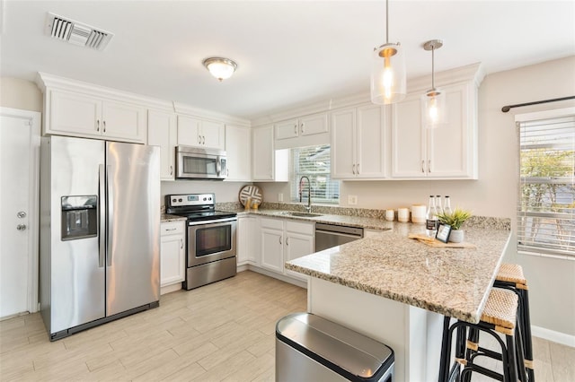 kitchen with appliances with stainless steel finishes, decorative light fixtures, kitchen peninsula, and white cabinets