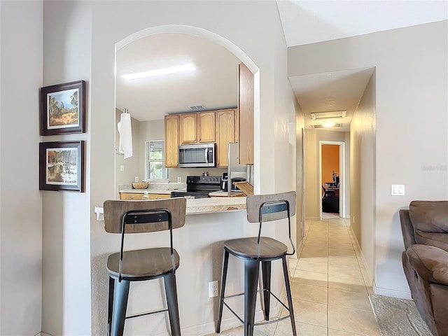 kitchen featuring light tile patterned flooring, light brown cabinetry, a breakfast bar area, kitchen peninsula, and stainless steel appliances