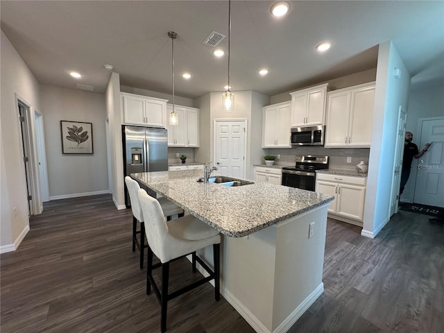 kitchen with appliances with stainless steel finishes, white cabinetry, an island with sink, sink, and light stone counters