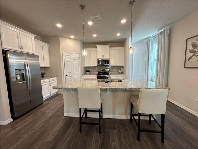 kitchen featuring appliances with stainless steel finishes, a kitchen island with sink, white cabinets, and decorative light fixtures