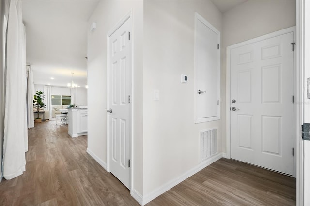 corridor featuring an inviting chandelier, wood finished floors, visible vents, and baseboards